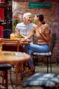 Mother and adult young daughter sitting in outdoor cafe, hugging each other, smiling