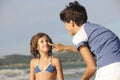 Mother applying sunscreen to daughter at beach.