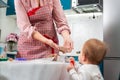 A mother in an apron shows a small child a cookie. The concept of home cooking and cooking together with children