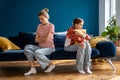 Young mother with arms crossed sits alone with offended teenage girl on couch who hugs pillow Royalty Free Stock Photo