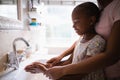 Mother assisting daughter while washing hands at bathroom sink