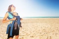 Mother and baby in carrier on the sunny sea beach Royalty Free Stock Photo