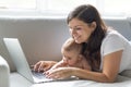 Mother and baby child are looking to play and read computer on the couch at home Royalty Free Stock Photo