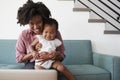 Mother With Baby Daughter Sitting On Sofa At Home Looking At Laptop Computer