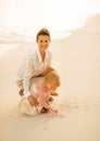 Mother and baby girl drawing on sand on beach Royalty Free Stock Photo