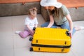 Mother and baby girl with yellow suitcase baggage and clothes, family ready for traveling on vacation at home Royalty Free Stock Photo