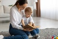 Mother baby leisure. Caring young mom reading book to her toddler son at home, relaxing together on floor carpet Royalty Free Stock Photo