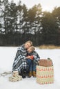 Mother and baby sitting on wooden sledge in winter forest and drinking hot tea. Christmas gifts presents on the snow Royalty Free Stock Photo