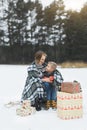 Mother and baby sitting on wooden sledge in winter forest and drinking hot tea. Christmas gifts presents on the snow Royalty Free Stock Photo