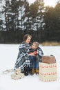 Mother and baby sitting on wooden sledge in winter forest and drinking hot tea. Christmas gifts presents on the snow Royalty Free Stock Photo