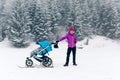 Mother with baby stroller enjoying motherhood in winter forest Royalty Free Stock Photo