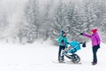 Mother with baby stroller enjoying winter forest with female friend or partner, family time. Hiking or power walking woman with Royalty Free Stock Photo