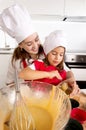 Mother baking with little daughter in apron and cook hat filling mold muffins with chocolate dough Royalty Free Stock Photo