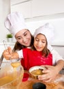 Mother baking with little daughter in apron and cook hat filling mold muffins with chocolate dough Royalty Free Stock Photo