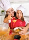 Mother baking with little daughter in apron and cook hat filling mold muffins with chocolate dough Royalty Free Stock Photo