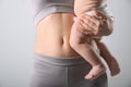 Mother with bare belly holding her baby on light grey background, closeup