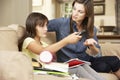 Mother Becoming Frustrated As Daughter Watches TV Whilst Doing Homework Sitting On Sofa At Home Royalty Free Stock Photo