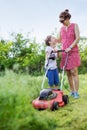 Mother and boy talking and laughing while mowing grass with lawn mower Royalty Free Stock Photo