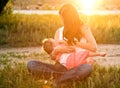 Mother breast feeding baby outdoors. Summer sunset.