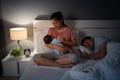 mother breastfeeding newborm baby while her husband sleeping on bed at night Royalty Free Stock Photo