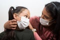 Mother cares for and puts the medical mask on her daughter to prevent illness. Woman wears a smart watch. Little girl looks to her