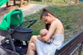 Mother caring baby in loving arms, breastfeeding baby in public sitting on wooden bench