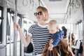 Mother carries her child while standing and holding on to bar holder on bus. Mom holding infant baby boy in her arms Royalty Free Stock Photo