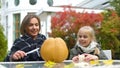 Mother carves pumpkin jack-o-lantern, daughter holding candle, togetherness