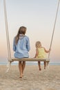 Mother chatting with little girl on swing and watch the stunning sunset over the sea. Magical sunrise over sea Royalty Free Stock Photo