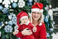 Mother with child baby boy with blue eyes in red costume and Santa Claus hat by New Year tree Royalty Free Stock Photo