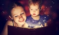 Mother and child baby daughter reading magic book in dark