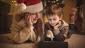 Mother with child on Christmas eve using digital tablet computer next to Christmas tree. Pure emotions of families and