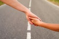 Mother and child hold hands together while walking along the highway in summer outdoors