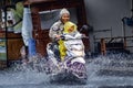 a mother and child on a motorbike wearing raincoats drive through flood waters during heavy rain in a residential area