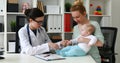 Mother with child at pediatrician reception in white room, checking motility skills of child.