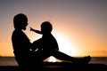 Mother and child playing and watching sunset on the beach in silhouette Royalty Free Stock Photo