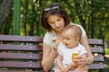 Mother and child together: young mom feeding her little baby child with vegetable puree on spoon in park. Happy motherhood Royalty Free Stock Photo