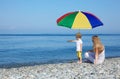 Mother with child under umbrella on pebble beach Royalty Free Stock Photo