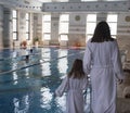 A woman with a daughter in white bathrobes around the swimming pool