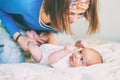 Mother and child on a white bed. Mom and baby boy in diaper playing in sunny bedroom. Mom makes gymnastics for her newborn baby. Royalty Free Stock Photo