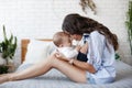 Charming happy little baby boy having fun with mom brunette woman on bed in the bright bedroom Royalty Free Stock Photo