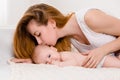 Mother and child on a white bed. Mom and baby girl in diaper playing in sunny bedroom. Royalty Free Stock Photo