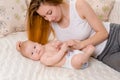 Mother and child on a white bed. Mom and baby girl in diaper playing in sunny bedroom. Royalty Free Stock Photo