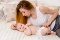 Mother and child on a white bed. Mom and baby girl in diaper playing in sunny bedroom. Royalty Free Stock Photo