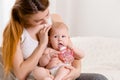 Mother and child on a white bed. Mom and baby girl in diaper playing in sunny bedroom. Royalty Free Stock Photo