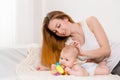 Mother and child on a white bed. Mom and baby girl in diaper playing in sunny bedroom. Royalty Free Stock Photo