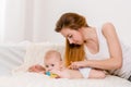 Mother and child on a white bed. Mom and baby girl in diaper playing in sunny bedroom. Royalty Free Stock Photo