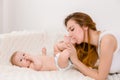 Mother and child on a white bed. Mom and baby girl in diaper playing in sunny bedroom. Royalty Free Stock Photo