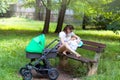 Mother and child, young mom is parenting her little toddler, woman breastfeeding and holding her baby, sitting on a park bench Royalty Free Stock Photo