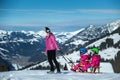 Mother and children having fun on sledge with panoramatic view of Alps mountains. Active mom and toddler kid with safety helmet. Royalty Free Stock Photo